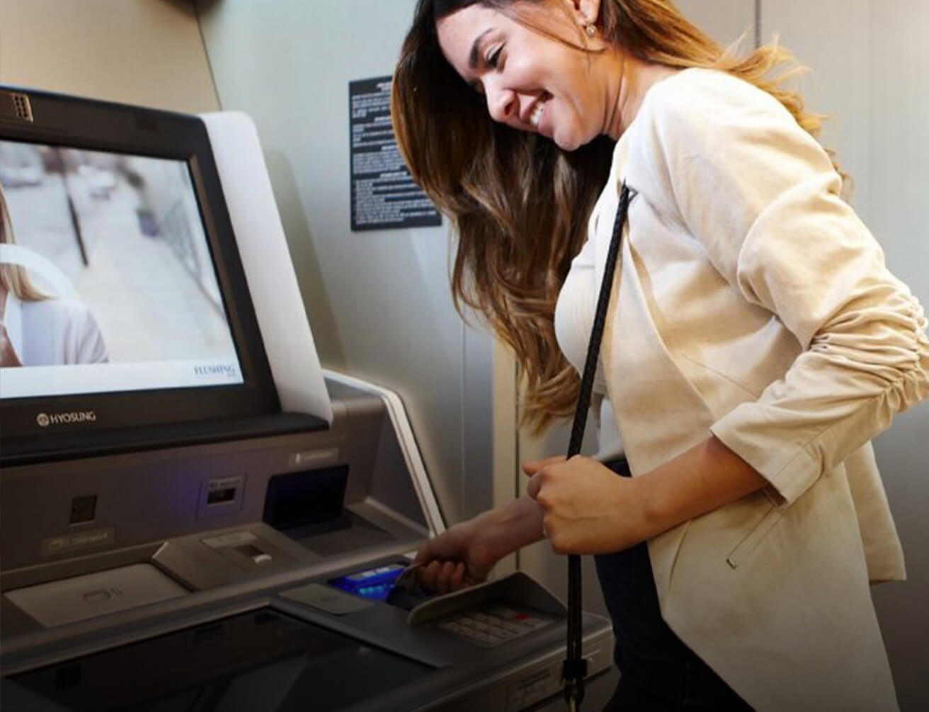 Woman wearing beige jacket using card at ATM